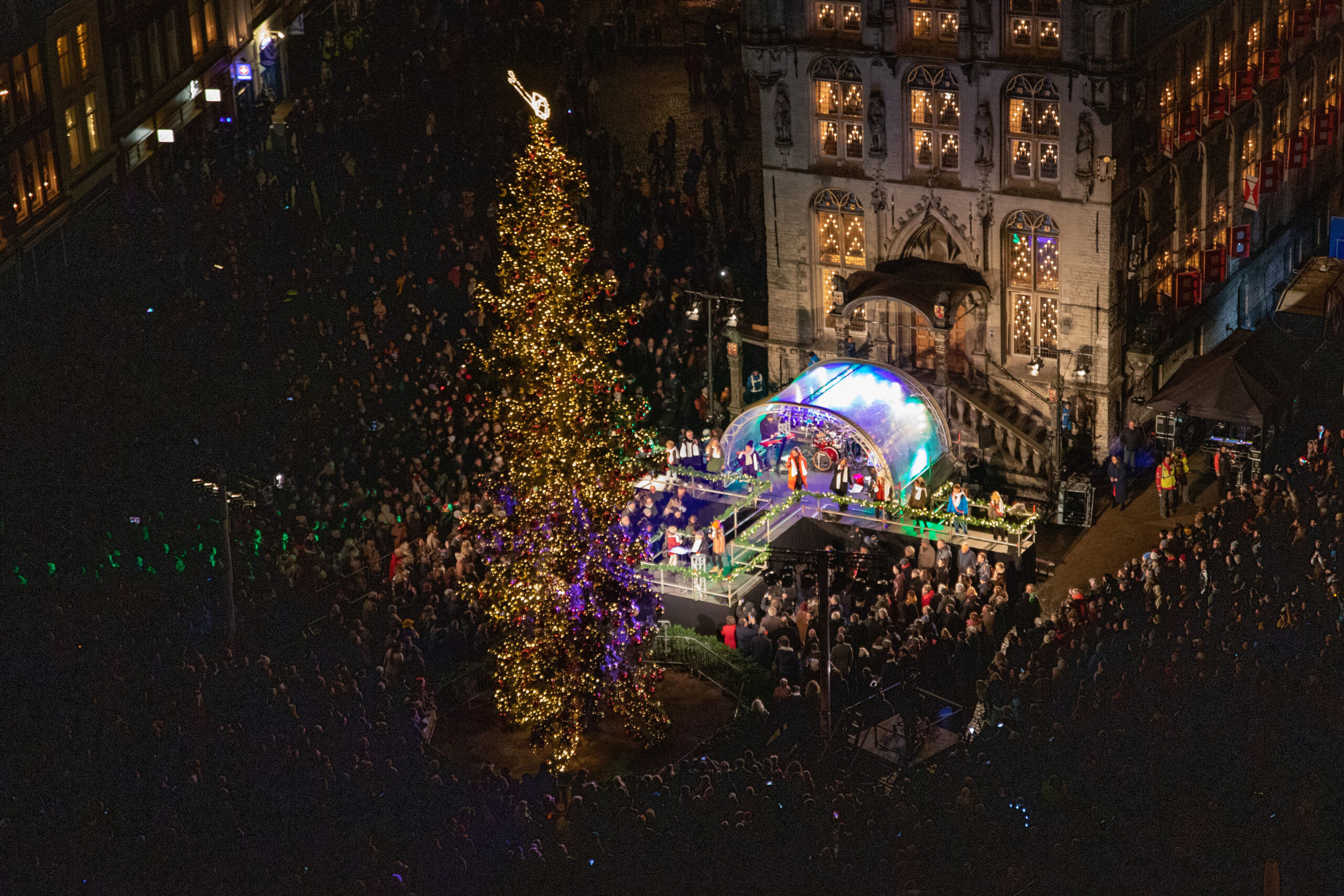 Podium voor het stadhuis, er wordt opgetreden en de kerstboom staat versierd en met de lichtjes aan.