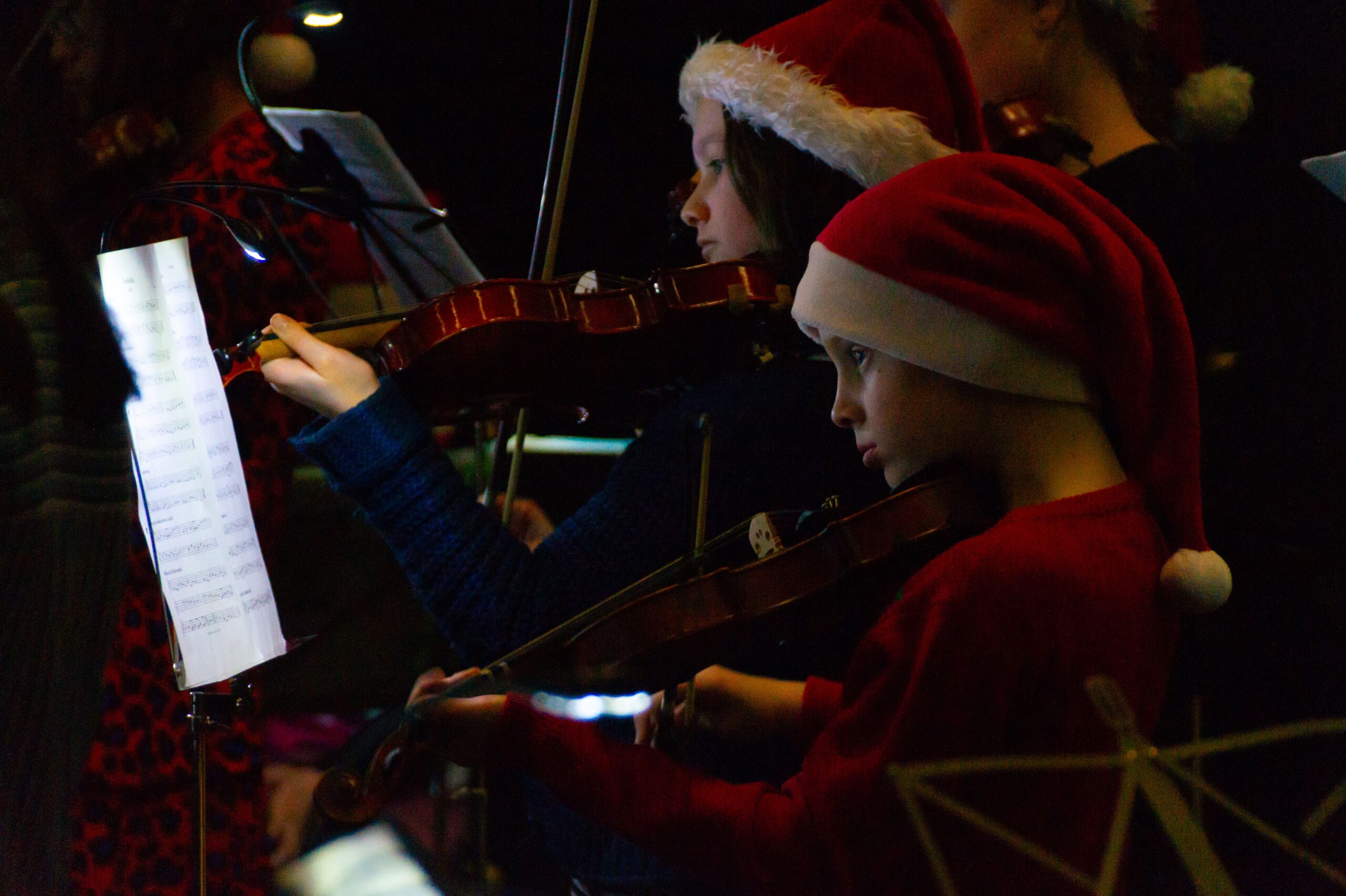 Foto van kinderen in een orkest. De kinderen spelen op een viool en hebben een kerstmuts op. 