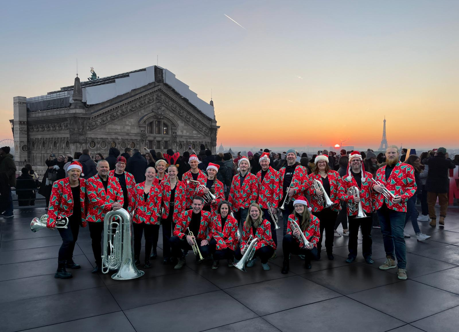 Groepsfoto van Jubal in Parijs met de Eiffeltoren op de achtergrond. Iets links daarvan gaat de zon net onder. 