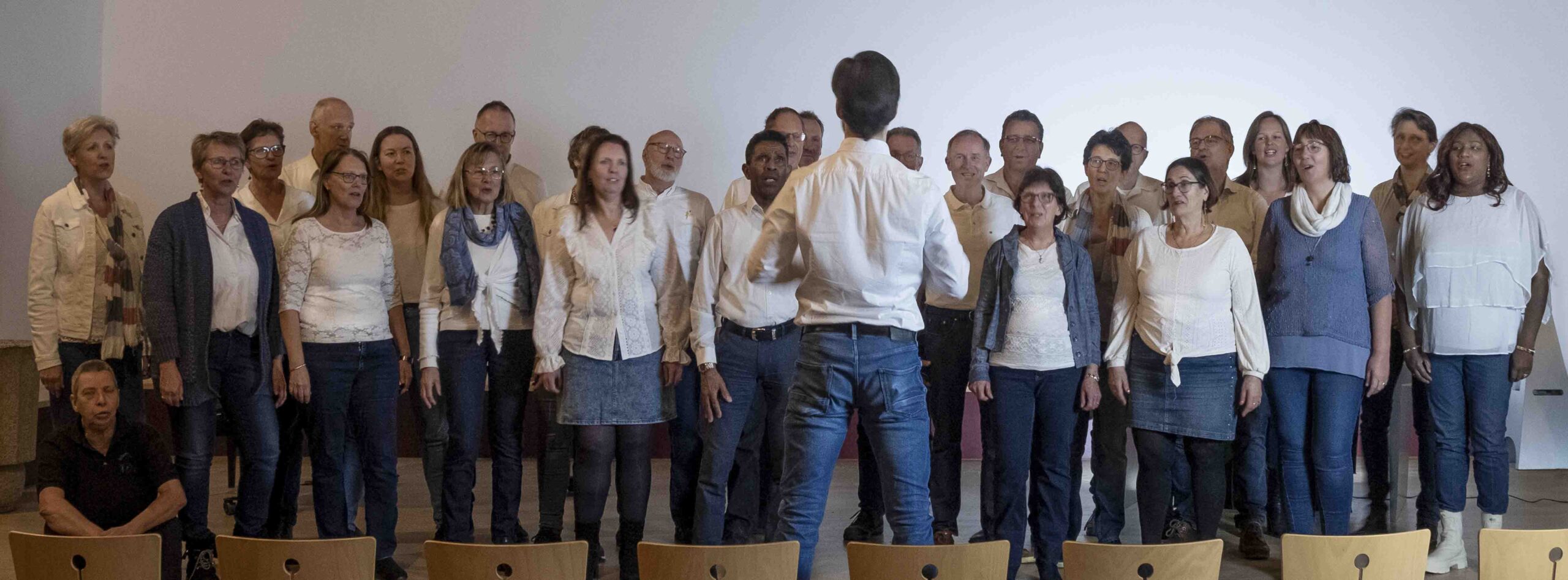 Foto van het koor Intercession, allen gekleed in wit -blauw. Voor de groep staat een dirigent. 