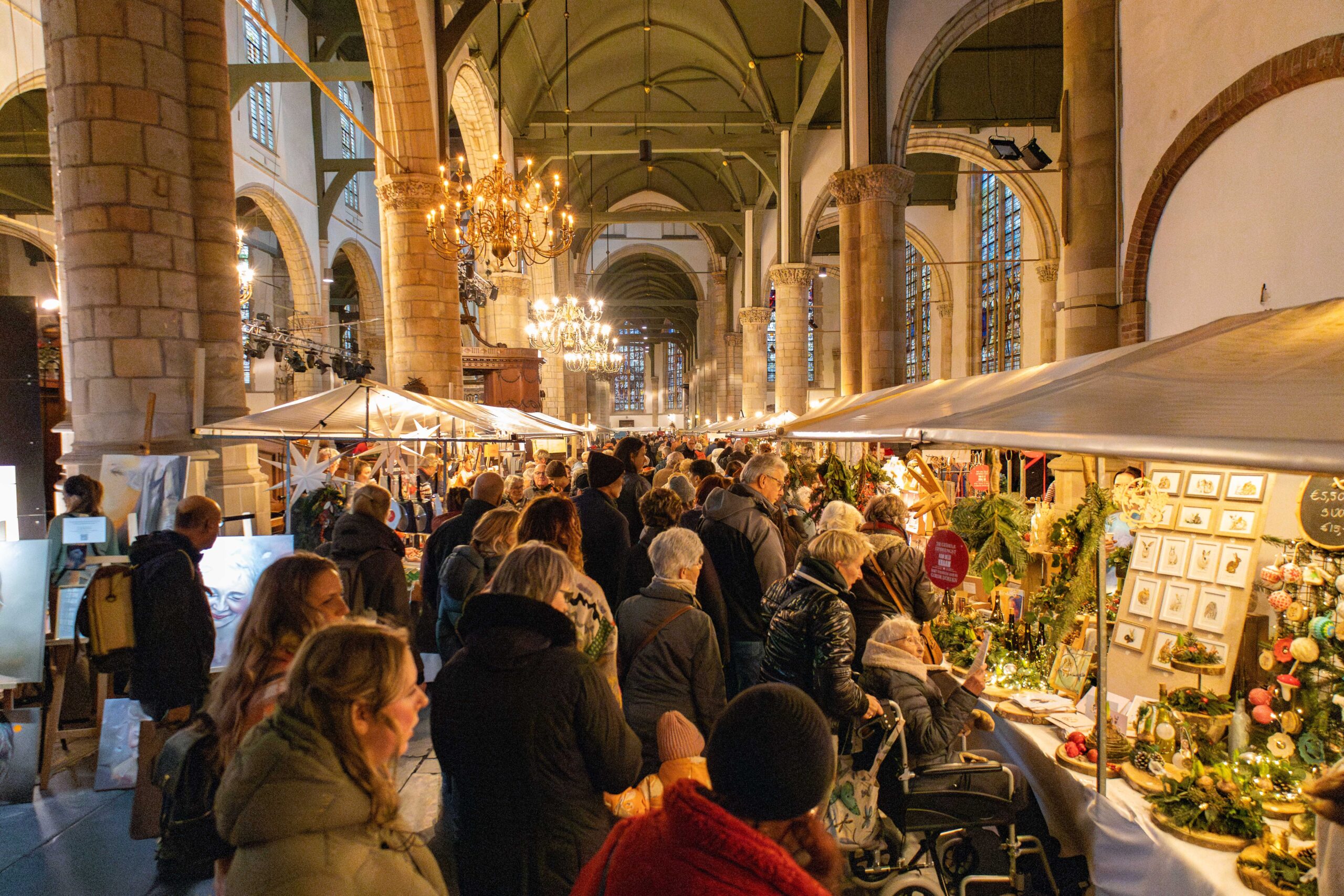 Mensen staan bij een kraampje in sfeervol verlichte Sint Janskerk in kerstsfeer